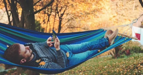 Man Relaxes, Uses Smartphone in a Hammock in Autumn. SLOW MOTION. Stock Footage 140321869