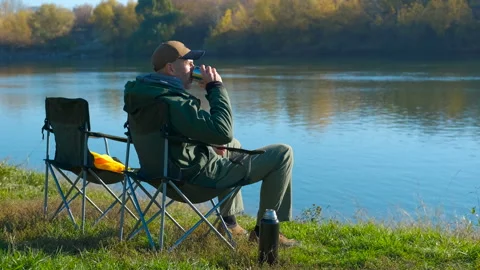 Man relaxing and drinking hot tea by the river Stock Footage 344854781