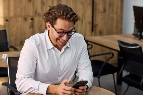 Man relaxing and using phone in outdoor cafe setting with wooden table and metal Stock Photos