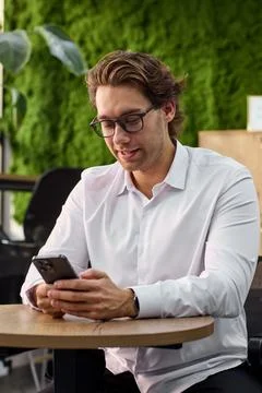 Man relaxing and using phone in outdoor cafe setting with wooden table and metal Stock Photos