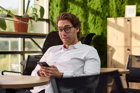 Man relaxing and using phone in outdoor cafe setting with wooden table and metal Stock Photos
