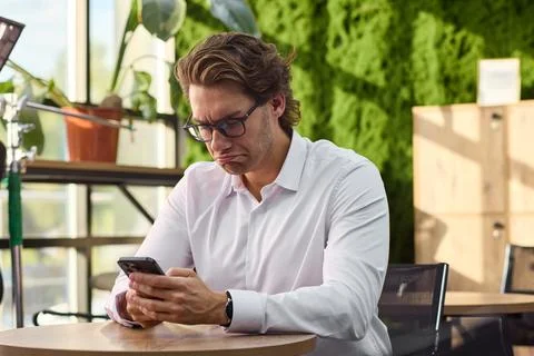 Man relaxing and using phone in outdoor cafe setting with wooden table and metal Stock Photos