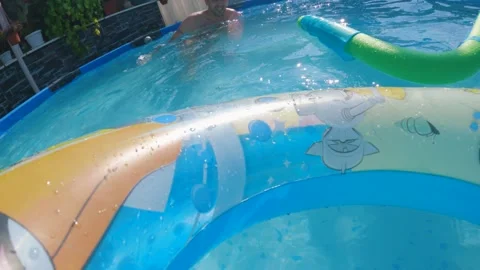 Man relaxing in a backyard swimming pool throws a child inflatable Stock Footage 241900482