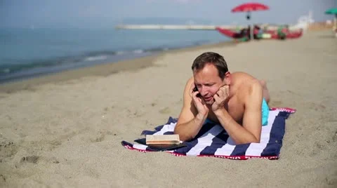Man relaxing on the beach and talking on a cell phone Stock Footage 12572647