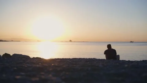 Man relaxing on beach looking at sun rising in sky Stock Footage 133263948