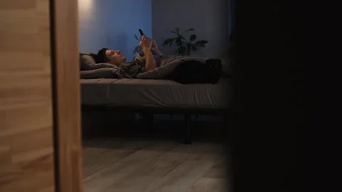 Man relaxing in bed at night, scrolling through his phone to unwind after work.  Stock Footage 296058488