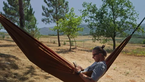Man relaxing with a book in a mountain hammock Видео 343656553