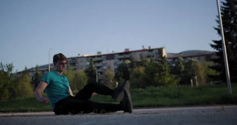 Man relaxing on the ground in a park as the sun sets behind urban buildings Stock Footage 346651789