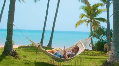 Man relaxing in a hammock between palm trees on tropical beach with turquoise Stock Footage 312814076