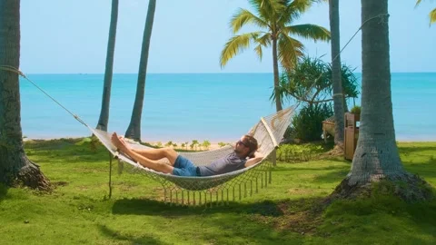 Man relaxing in a hammock between palm trees on tropical beach with turquoise Stock Footage 312814114