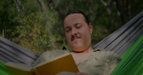 Man Relaxing In A Hammock Outdoors While Reading... 库存影片 331820777