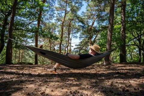 Man Relaxing In Hammock In Pine Forest On Sunny Day Wearing Straw Hat And Boo Stock Photos