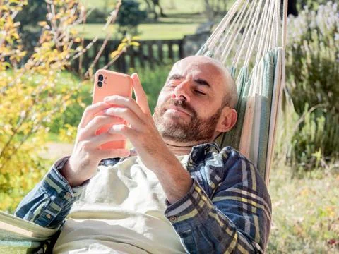 Man relaxing in hammock using smartphone outdoors Stock Photos