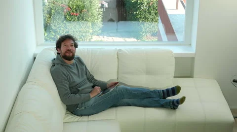 Man relaxing at home playing with tablet lying on sofa looking camera happy Stock Footage 60158230