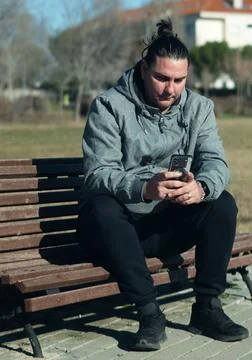 Man relaxing on park bench using smartphone Stock Photos
