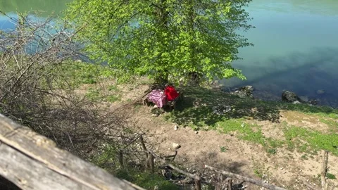 Man Relaxing at Rustic Picnic Table Under Tree Near River, Countryside Slow Livi Stock Footage 333523016