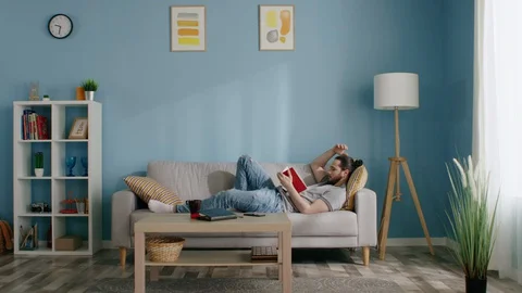 Man Is Relaxing on Sofa and Reading Book Stock Footage 129886497