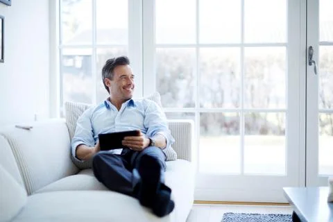 Man relaxing on sofa using digital tablet Stock Photos