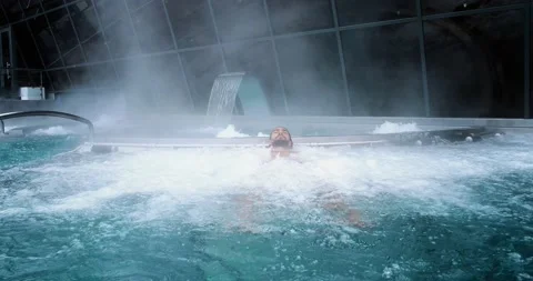 Man relaxing in a spa, he is lying in the water with steam all around him. Perfe Vídeos de archivo 143629909