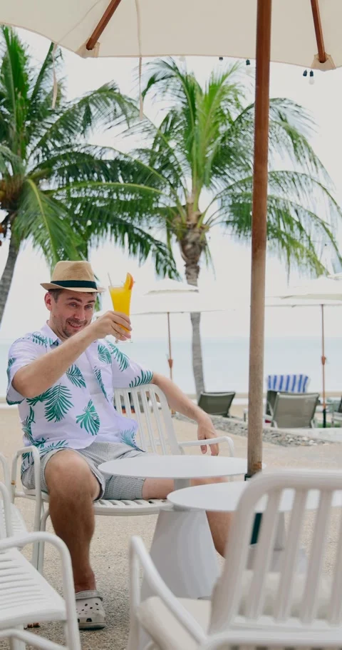 Man relaxing at tropical beach resort, sitting under umbrella with Stock Footage 314043853