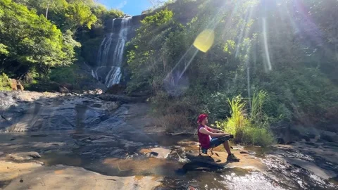 Man Relaxing by Waterfall and River in Lush Forest, Panning Shot 스톡 동영상 324770204