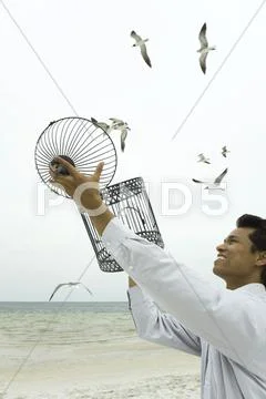 Man Releasing Bird At The Beach, Empty Bird Cage In Hands