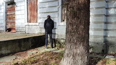 A man relieves himself and urinates on the corner of an abandoned building in Video stock 254064550