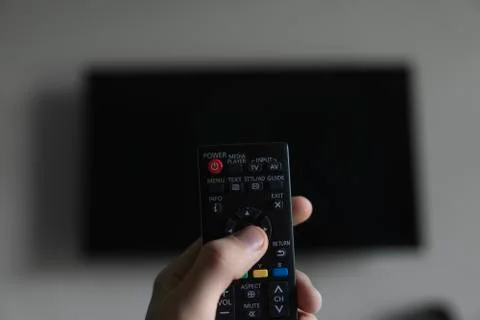 The man with the remote control in hand want switch on the TV and presses the Stock Photos
