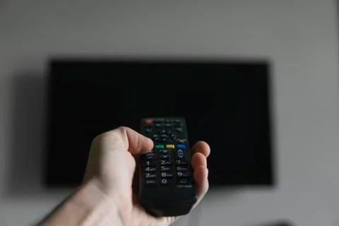 The man with the remote control in hand want switch on the TV and presses the Stock Photos