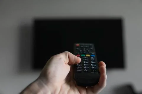 The man with the remote control in hand want switch on the TV and presses the Stock Photos