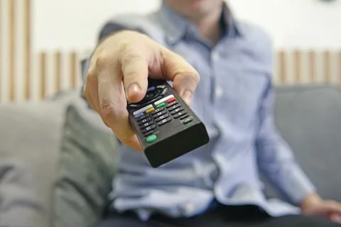 The man with remote control in hand watching the sports channel and presses t Stock Photos