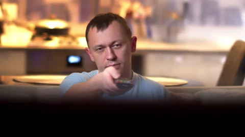 A man with a remote control in hands sits on the couch and watches TV Stock Footage 136329684