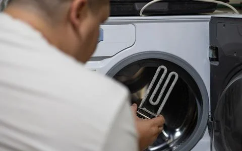 A man removed an old heating element from a broken washing machine and inspects Stock Photos