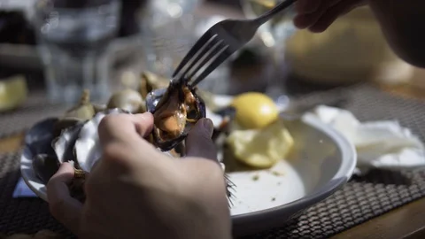 Man removes a mussel from its shell with a fork and sprinkles fresh lemon juice Stock Footage 106247057
