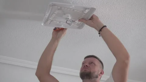 A man removes an old ceiling light fixture using tools during home renovation Stock Footage 316386043