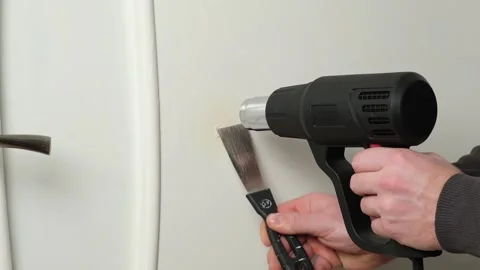 A man removes old white enamel paint from wooden door with a construction hair Видео 171637874