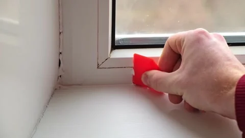 The man removes the silicone sealant between the window and sill with a rubber Stock Footage 168323369