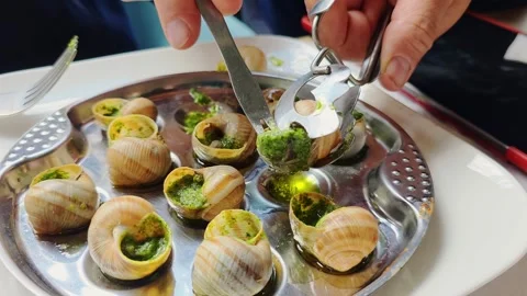 Man removes a snail from its shell using special tongs and a fork at a Fren.. Vídeos de archivo 340469285