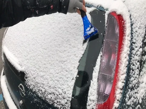 A man removes snow from the windshield of a car in a street while snowing. Stock-Footage 83659677