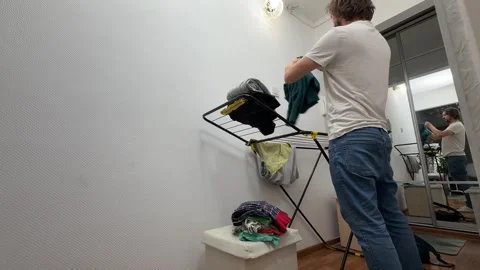 Man removing clean clothes from drying rack at home, laundry routine, household Stock Footage 335645748