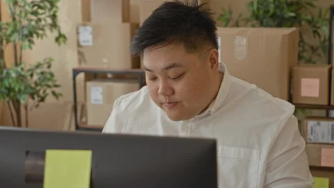 Man removing glasses and rubbing eyes at computer with stacked shipping box.. Stock Footage 337390314