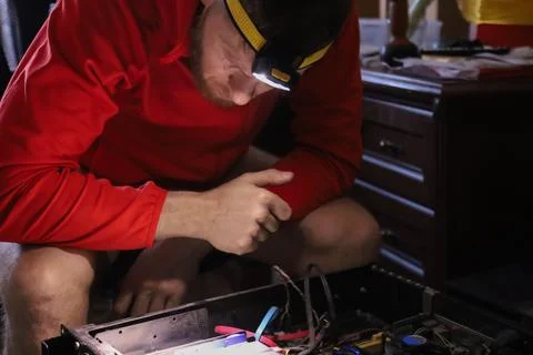 Man repairing computer hardware with headlamp in workshop Stock Photos