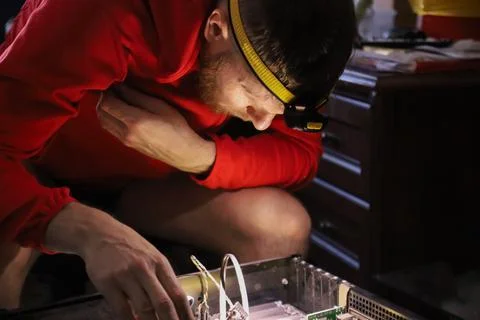 Man repairing computer hardware with headlamp in dark room Stock Photos