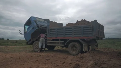 Man repairing a small truck loaded with earth and with his cab tilted forward Stock Footage