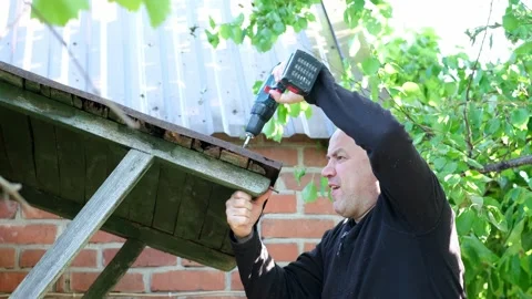 Man repairs canopy of an old small house. Male works with screwdriver outdoors Stock-Footage 199922374
