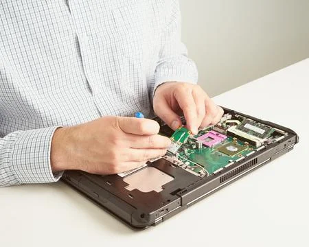 Man repairs computer. A service engineer in shirt repairs laptop, at white .. Stock Photos