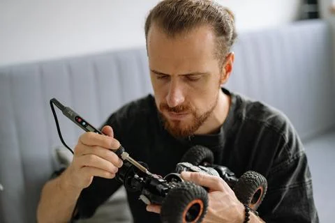 Man repairs remote control car inside home while focused on soldering with Stock Photos