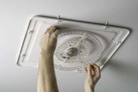 Man replaces LED ceiling module on white panel, careful hands show safe home 写真素材