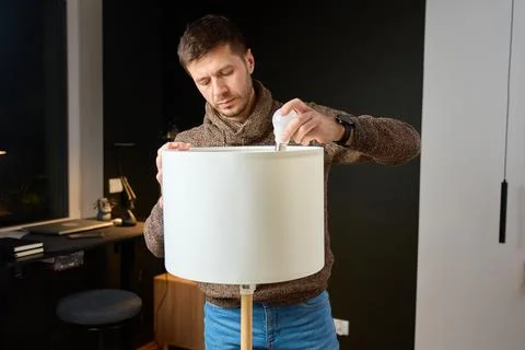 Man replacing light bulb in floor lamp while standing in home interior 写真素材