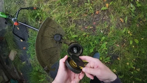 Man replacing trimmer line in powerful electric grass trimmer first person .. Stock Footage 340143506